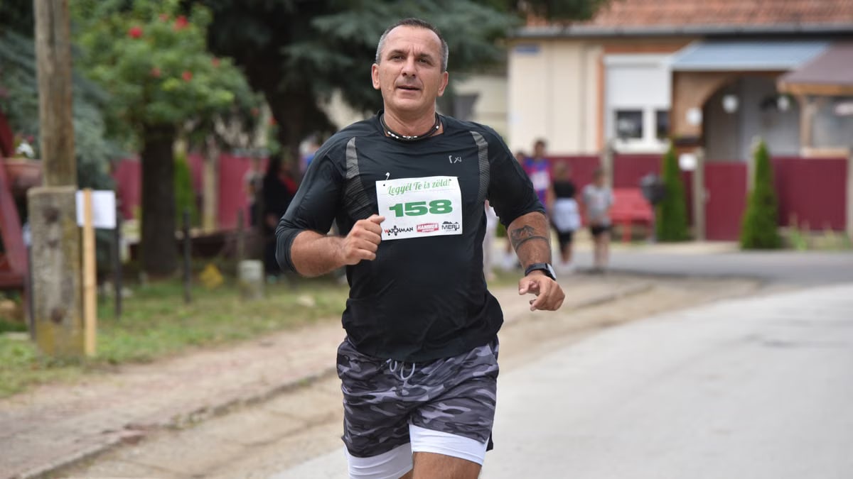Middle-aged man jogging in a marathon event, wearing a number bib on an outdoor suburban street.
